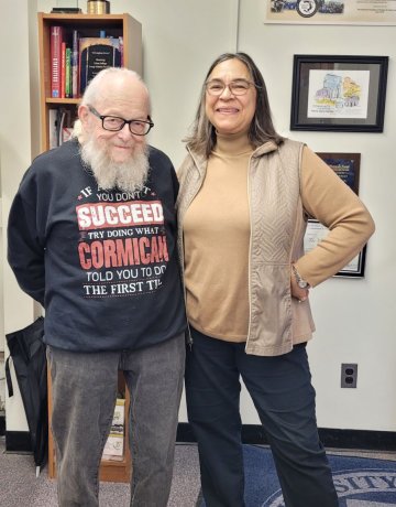 John Cormican in a sweatshirt that reads "if at first you don't succeed, try doing what Cormican told you to do the first time," stands with former student Mary Hayes Gordon.