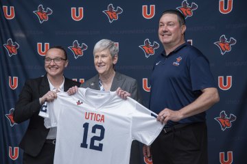 Kristin St. Hilaire, Stephanie Nesbitt, and Damian Boehlert hold up a Utica Pioneers jersey.