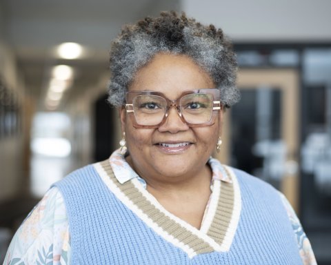 Joanne Johnson, in glasses and a blue sweater vest smiles at the camera.