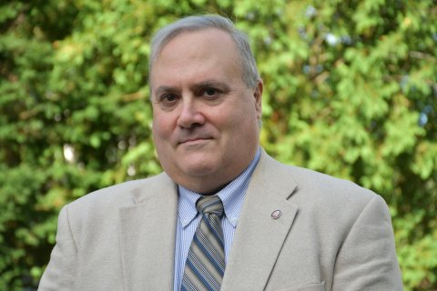 James Teliha in tan jacket, blue shirt, and and striped tie.