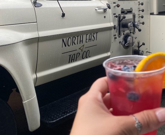 Hand holds a drink in front of the North East Tap Company Beer Truck.
