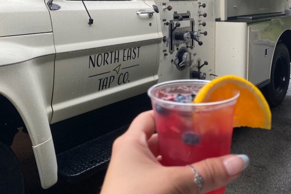 Hand holds a drink in front of the North East Tap Company Beer Truck.