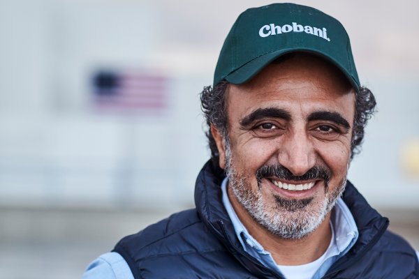 Hamdi Ulukaya, founder and CEO of Chobani, in a Chobani hat and blue vest, smiles at the camera.