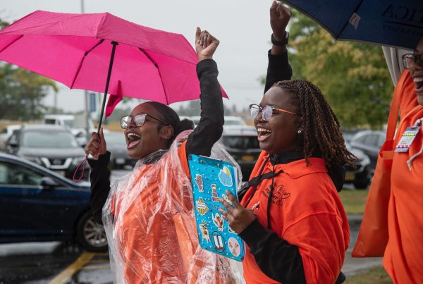 Two students under umbrellas shout excitedly with arms in the air and smiles on their faces as they greet new students.