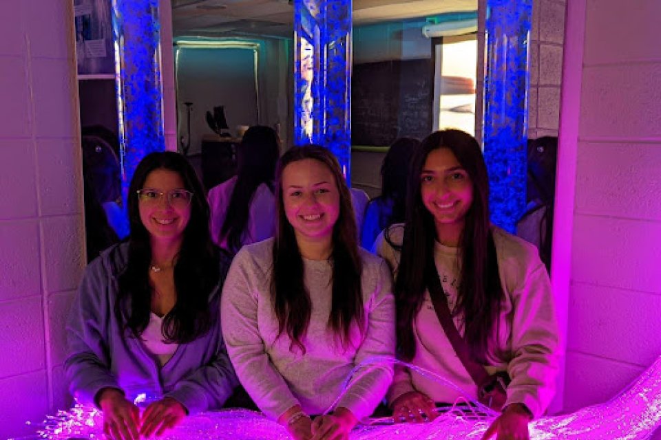 Three students sit in the Utica University Sensory Room, with purplish-blue lights on.